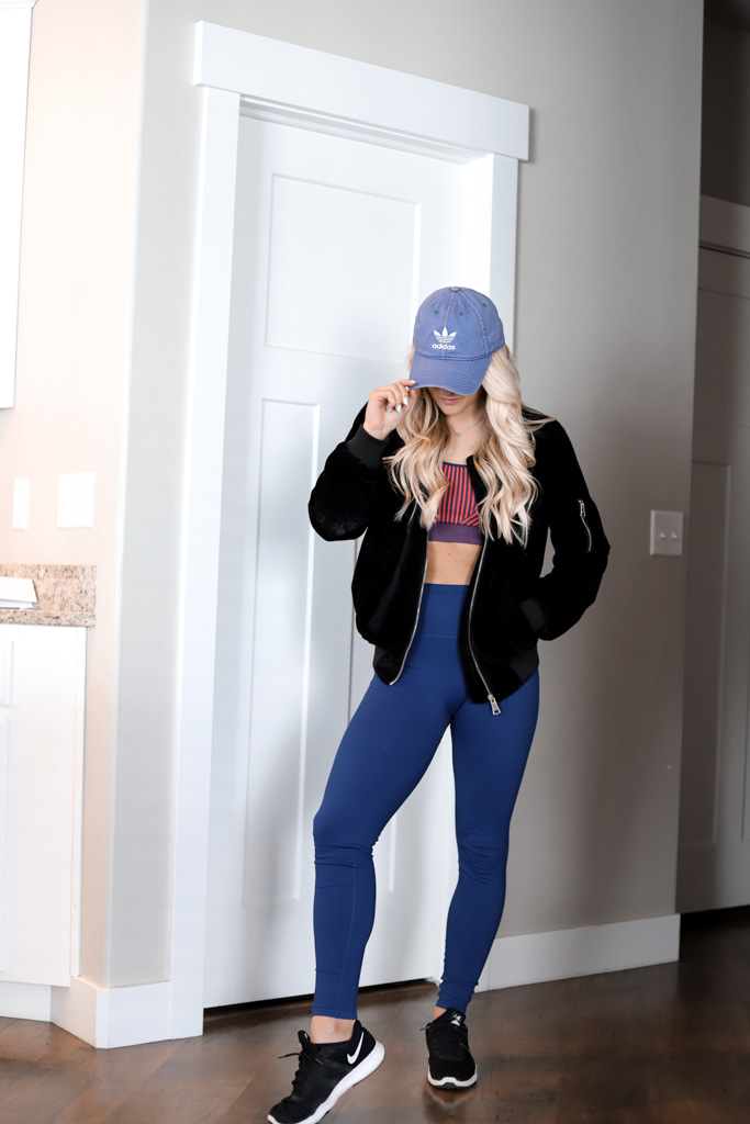 girl in navy blue leggings and matching sports bra. A black velvet jacket with an adidas hat.