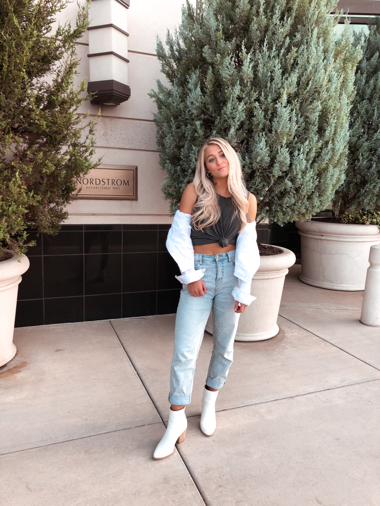 girl standing in front of tree wearing mom jeans and whit denim jacket off the shoulder