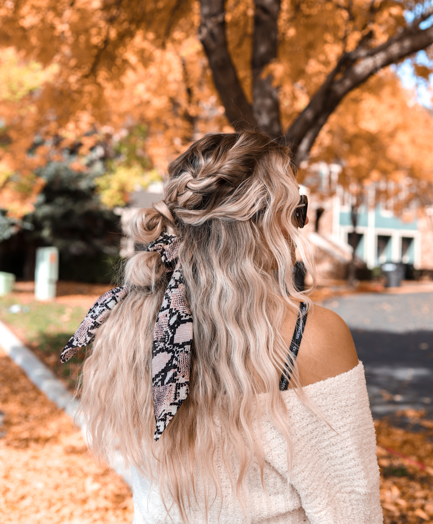 wavy hair and snake skin print hair tie. She's in front of a yellow fall tree.