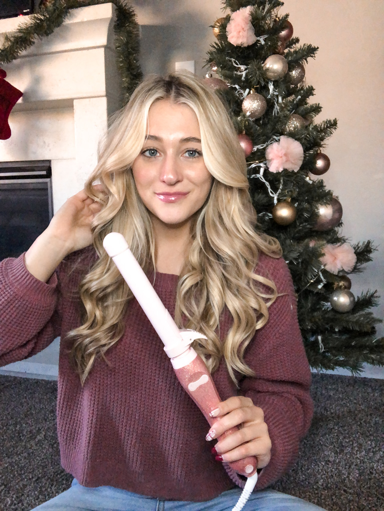 girl holding a curling iron in front of a christmas tree
